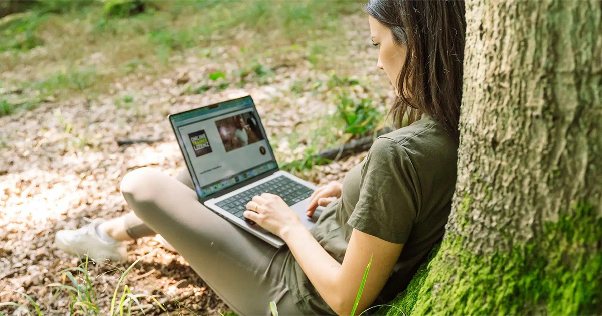 woman sitting against tree with laptop