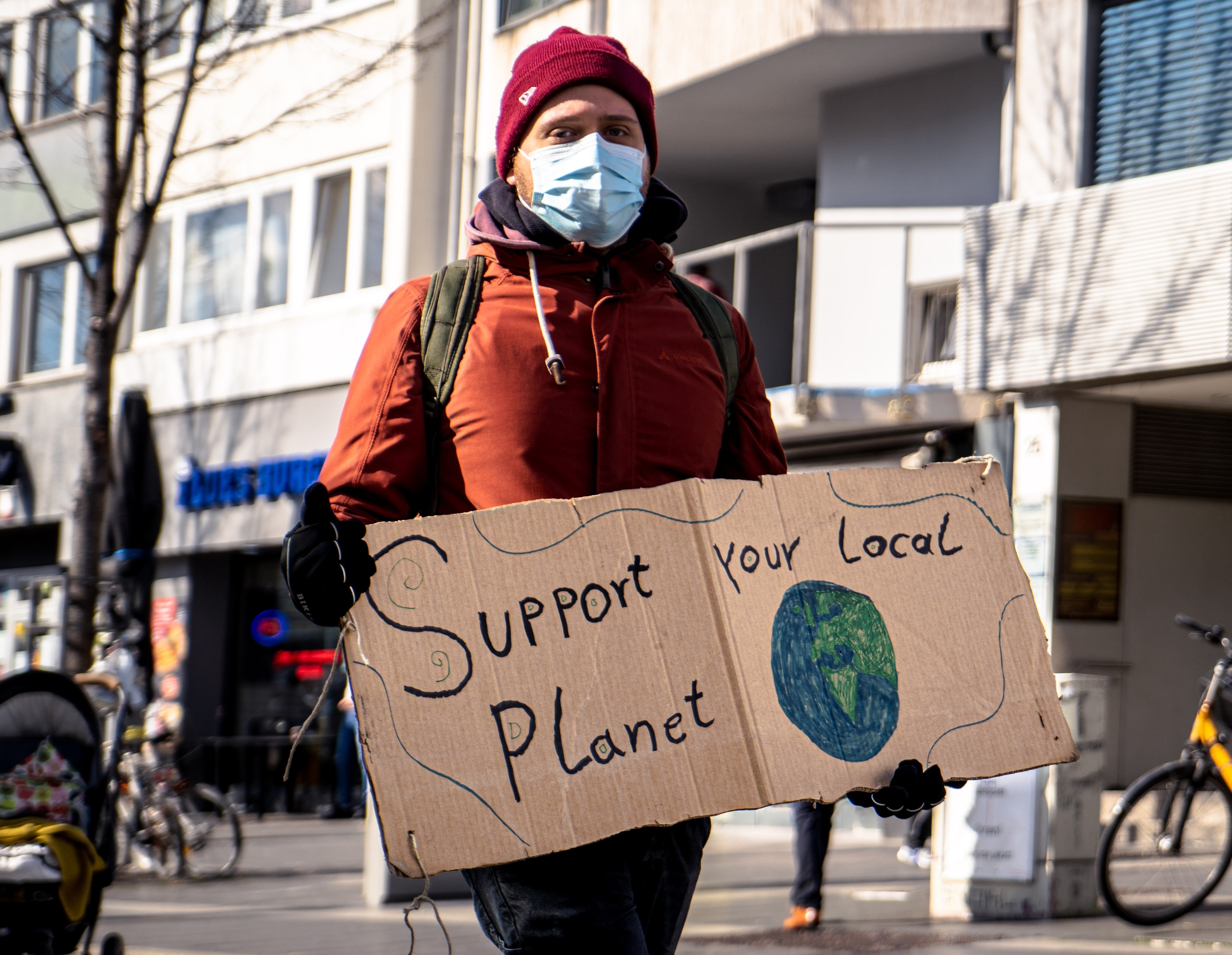 man holding cardboard sign saying support your local planet
