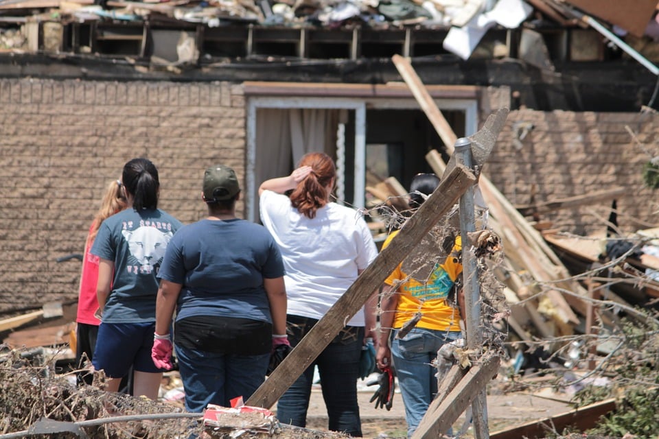 five women standing in front of house destroyed by tornado